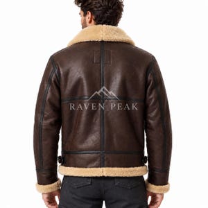 Puede incluir: Una chaqueta de cuero marr&oacute;n oscuro con cuello, pu&ntilde;os y dobladillo de borrego beige. La parte trasera presenta costuras negras, hebillas de ajuste laterales y el texto RAVEN PEAK impreso en blanco con un logo de monta&ntilde;a encima.