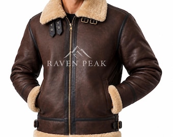May include: A dark brown jacket with a thick beige shearling collar, cuffs, and hem. The jacket features a gold-tone front zipper, black leather trim, and adjustable side buckles. The text RAVEN PEAK is printed on the chest with a mountain logo.