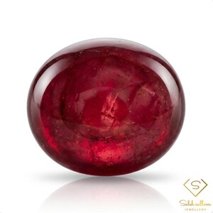 May include: A round, polished, deep red gemstone with a smooth, cabochon-style surface. The stone displays internal natural inclusions and fractures throughout its translucent body. In the bottom right corner, the text reads Saleh sallom JEWELLERY.