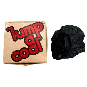 May include: A square cardboard box with the text "lump a coal" printed in bold red letters on the front, accompanied by a single, irregular, jagged piece of black coal positioned to the right of the box.