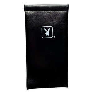 May include: A rectangular black protective case with a smooth, leather-like texture. Centered on the front is a white graphic of the Playboy rabbit head logo inside a rounded square, accompanied by a small registered trademark symbol.