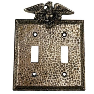 May include: A double light switch wall plate with a hammered metal texture and a silver finish. The top edge features a decorative eagle emblem with spread wings. The rectangular plate includes four screw holes and two vertical rectangular cutouts.