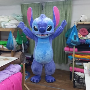 Peut inclure: Un costume int&eacute;gral du personnage Stitch du film d'animation Lilo & Stitch. Le costume est principalement bleu avec de grandes oreilles, un ventre rond et de grands pieds. Le personnage sourit, les bras lev&eacute;s.