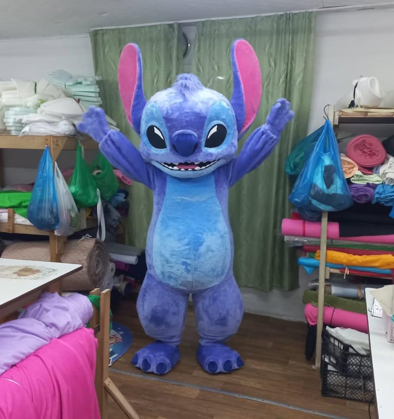 Peut inclure: Un costume int&eacute;gral du personnage Stitch du film d'animation Lilo & Stitch. Le costume est principalement bleu avec de grandes oreilles, un ventre rond et de grands pieds. Le personnage sourit, les bras lev&eacute;s.