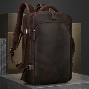Puede incluir: Una mochila de cuero marrón oscuro que presenta un compartimento principal grande con un bolsillo frontal con cremallera, correas laterales ajustables con hebillas metálicas, un asa superior y correas acolchadas con forro de malla.