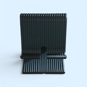 May include: A black, ribbed phone stand with a rectangular base and a slot to hold a phone. The stand is made of a dark, matte material and has a series of vertical lines on the front and back.