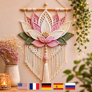 May include: A macrame wall hanging in the shape of a lotus flower. The flower features pink, cream, and green colours, with a wooden dowel at the top for hanging. A tassel hangs from the bottom. The wall hanging is a decorative piece.