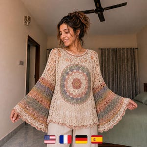 Könnte beinhalten: Ein cremefarbenes Häkeltop mit einem Mandala-Design auf der Vorderseite. Die langen Ärmel haben horizontale Streifen in Rosa-, Blau- und Grüntönen. Das Oberteil hat einen runden Ausschnitt und einen gewellten Saum. Das Model trägt eine beige Hose.