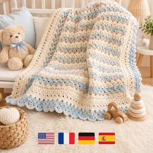 May include: A handmade, cream-colored crochet blanket with light blue and tan stripes. The blanket has a scalloped edge in light blue. A teddy bear and wooden toys are in the background. The blanket is approximately 40 inches wide and 50 inches long.
