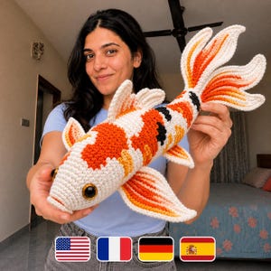 May include: A handmade crochet koi carp in orange, white, black, and yellow. The fish has large, detailed fins and a tail. The fish is approximately 46 cm long.