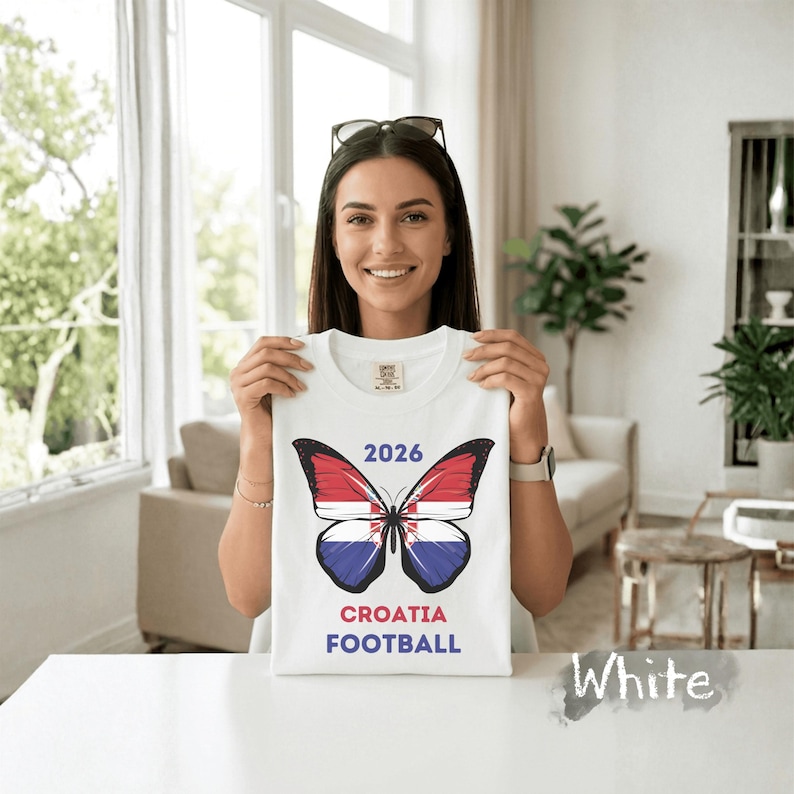 May include: A white t-shirt featuring a graphic of a butterfly with wings patterned like the Croatian flag. Above the butterfly is the text 2026, and below the butterfly is the text CROATIA FOOTBALL in red and blue lettering on the front center.