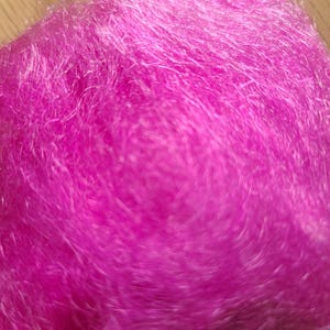 May include: A vibrant, hot pink fibrous material with a dense, tangled, and translucent texture. The material consists of numerous thin, interlaced strands that create a soft, voluminous, and cloud-like appearance with varying light reflections.