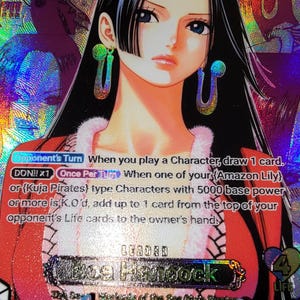 以下が含まれることがあります： 長い黒髪で、白いファーの襟が付いた赤い衣装と大きな緑のイヤリングを身に着けたボア・ハンコックが描かれた、ホログラフィック仕様のワンピーストレーディングカード。カードにはゲームテキスト、パワー5000、ボア・ハンコックの名前が記載されています。