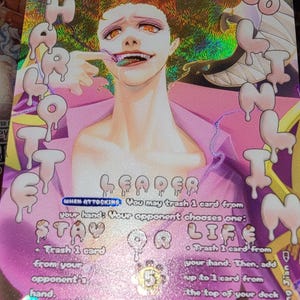 Pode incluir: Uma carta colecionável holográfica apresentando a personagem Charlotte Linlin com cabelo rosa e olhos laranja. A carta exibe o texto Leader, 5000 power e instruções de jogo incluindo When Attacking, Stay or Life e Big Mom Pirates.