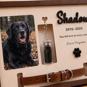 May include: A rectangular wooden memorial frame featuring a photo of a black Labrador, a small glass vial on a metal keychain, and a brown leather collar. The text reads Shadow, 2010-2025, You left love in every corner, and Never Forgotten.