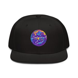 May include: A black baseball cap featuring a circular graphic on the front panel. The graphic displays a swirling, psychedelic pattern in shades of purple, blue, and yellow, with the text Spaced Out written in a bold, purple, cursive font.