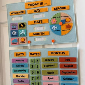 K&ouml;nnte beinhalten: Ein hellblaues Lernkalender aus Filz mit orangefarbenem Text und farbigen Filzteilen. Der Kalender enth&auml;lt Abschnitte f&uuml;r Wetter, Tag, Datum, Monat und Jahreszeit. Er hat auch Abschnitte f&uuml;r Tage, Daten und Monate.