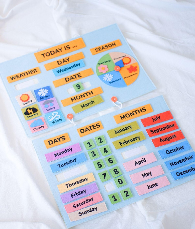 K&ouml;nnte beinhalten: Ein hellblaues Filz-Lernkalender mit orangefarbenen, gr&uuml;nen und rosa Etiketten. Er verf&uuml;gt &uuml;ber Abschnitte f&uuml;r Wetter, Tag, Datum, Monat und Jahreszeit. Enth&auml;lt Wettersymbole sowie Zahlen- und Monatsbezeichnungen.