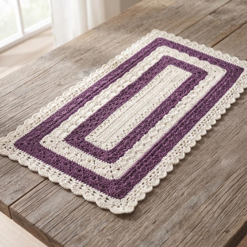 Puede incluir: Un mantel individual rectangular de ganchillo con bandas conc&eacute;ntricas alternas de hilo color crema y morado oscuro. El dise&ntilde;o incluye una secci&oacute;n central s&oacute;lida en color crema, un borde morado texturizado y un borde festoneado de encaje.