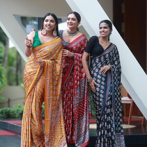 May include: Three sarees featuring intricate floral patterns and reflective mirror work. One saree is mustard yellow with a green blouse, one is deep red with a blue blouse, and one is black with a black blouse, all draped in traditional style.