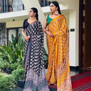 May include: Two sarees, one black with a white and pink floral pattern and a solid black blouse, and one mustard yellow with a white floral pattern and a solid green blouse. Both garments feature intricate borders and draped fabric silhouettes.