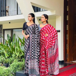 May include: Two sarees, one black with a white floral pattern and a black blouse, and one red with a white floral pattern and a blue blouse. Both garments feature intricate block-print designs, draped over the body with a long pallu end.