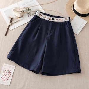 Puede incluir: Pantalones cortos azul marino de talle alto con una cinturilla blanca decorada con un estampado floral marr&oacute;n. Los pantalones incluyen un cierre de bot&oacute;n oscuro en la parte central delantera, dos bolsillos laterales y una silueta de pernera holgada.