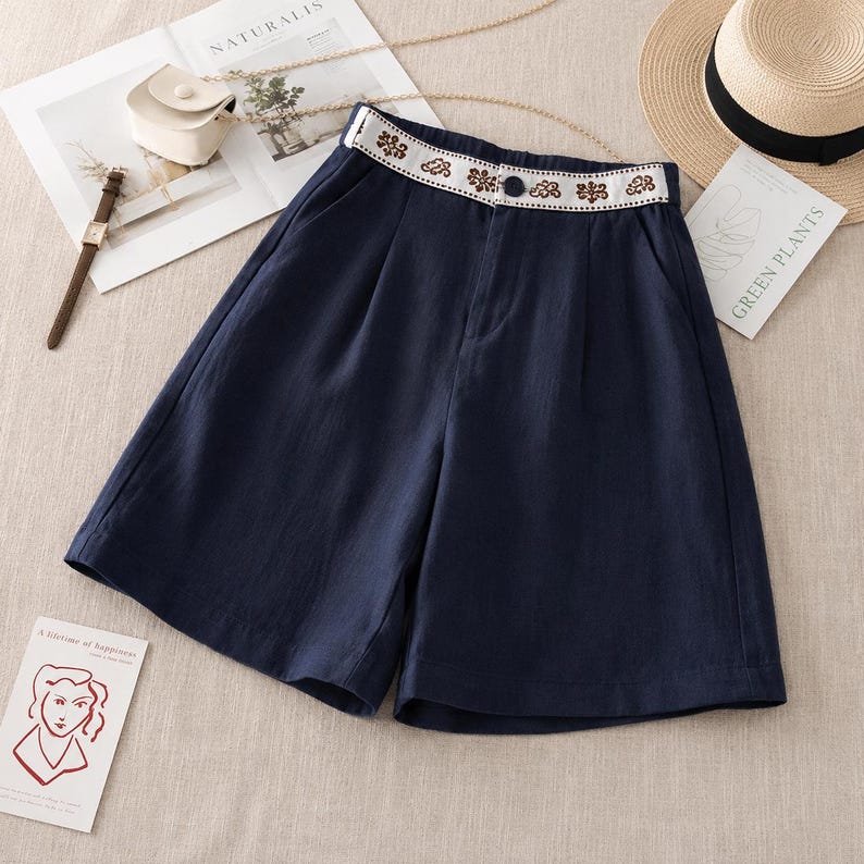 Puede incluir: Pantalones cortos azul marino de talle alto con una cinturilla blanca decorada con un estampado floral marr&oacute;n. Los pantalones incluyen un cierre de bot&oacute;n oscuro en la parte central delantera, dos bolsillos laterales y una silueta de pernera holgada.
