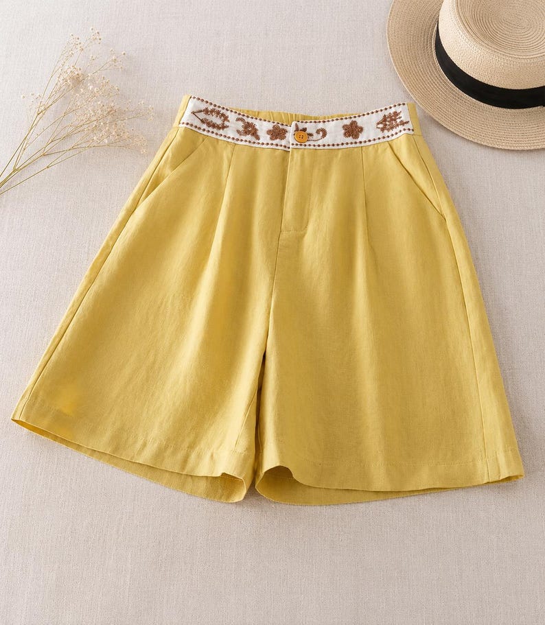 Puede incluir: Pantalones cortos de color amarillo mostaza con dise&ntilde;o de cintura alta, una banda blanca decorada con bordados florales marrones y un cierre de un solo bot&oacute;n amarillo. Tienen frente plisado, bolsillos laterales y pernera ancha.