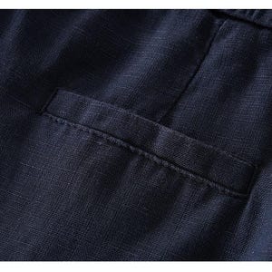 Puede incluir: Una vista de cerca de una prenda de color azul marino oscuro que presenta un bolsillo de ojal horizontal. La tela muestra una textura tejida visible con un patr&oacute;n entrecruzado, y la abertura del bolsillo tiene un borde de costura recto.