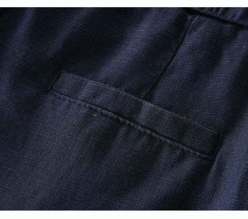 Puede incluir: Una vista de cerca de una prenda de color azul marino oscuro que presenta un bolsillo de ojal horizontal. La tela muestra una textura tejida visible con un patr&oacute;n entrecruzado, y la abertura del bolsillo tiene un borde de costura recto.
