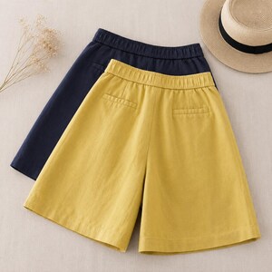 Puede incluir: Un par de pantalones cortos de color amarillo mostaza con cintura el&aacute;stica y dos bolsillos traseros, superpuestos sobre un par de pantalones cortos de color azul marino oscuro con cintura el&aacute;stica a juego, ambos de dise&ntilde;o sencillo.