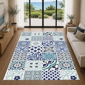 Può includere: Un tappeto rettangolare con un design patchwork con vari motivi geometrici blu e bianchi. Il tappeto è posto su un pavimento in legno in un soggiorno, con vista sul mare attraverso una grande finestra.