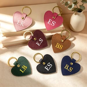 Puede incluir: Siete llaveros en forma de corazón de material texturizado en rosa, magenta, burdeos, marrón, verde oscuro, negro y azul marino. Cada uno tiene una anilla de metal dorado, un remache dorado e iniciales grabadas en blanco o dorado como LK, ES, BS y LB.