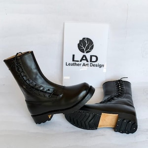 Op de afbeelding: Zwarte leren laarzen met vetersluiting en stevige zolen. De laarzen staan op een witte achtergrond, met het "LAD Leather Art Design" logo zichtbaar.