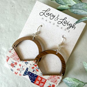 Puede incluir: Pendientes colgantes con una parte superior circular de madera oscura unida a una base semicircular con estampado floral en blanco, rojo y azul. Los pendientes se presentan en una tarjeta blanca con el texto Lucy & Leigh HANDMADE en negro.