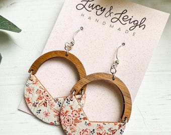 May include: A pair of handmade earrings with a wooden half-circle design. The lower half of each earring features a cream-colored material with a floral pattern in shades of red and orange. The earrings are labeled "Lucy & Leigh Handmade."