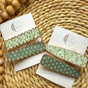 May include: Set of four green and white patterned hair clips with gold trim. The clips feature a floral pattern and a polka dot pattern. The clips are arranged on a white card with the text "Lucy & Leigh" printed on it.