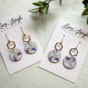 May include: Two pairs of dangle earrings on white display cards labeled Lucy & Leigh Handmade. Each earring features a gold or silver-toned hexagon connector attached to a circular pendant with a blue, pink, and white floral patchwork pattern.