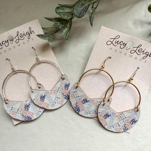 Puede incluir: Dos pares de pendientes colgantes en tarjetas de la marca Lucy & Leigh Handmade. Cada pendiente presenta una pieza semicircular con un patrón de patchwork floral azul, rosa y blanco unido a un aro de metal. Un par tiene aros plateados, el otro dorados.