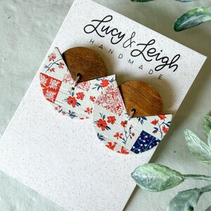 Puede incluir: Un par de pendientes en una tarjeta blanca con la etiqueta Lucy & Leigh Handmade. Cada pendiente presenta una parte superior de madera oscura semicircular unida a una base blanca con un patrón floral y geométrico en rojo y azul.