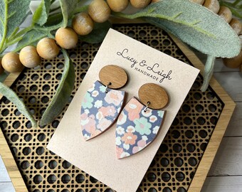 Può includere: Un paio di orecchini con motivo floreale in uno schema di colori blu chiaro, rosa e verde. Gli orecchini sono in legno e hanno un perno rotondo in legno. Gli orecchini sono esposti su una carta con il testo "Lucy & Leigh Handmade".