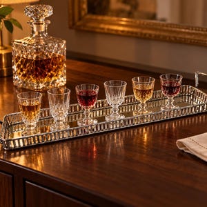 Peut inclure: Un plateau de service rectangulaire argenté à fond miroir avec deux poignées latérales, supportant six verres à pied transparents. Les verres présentent un motif extérieur taillé en diamant, certains contenant des boissons ambrées et rouges.