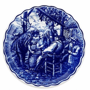 Può includere: Un piatto rotondo in ceramica con bordo smerlato caratterizzato da una stampa blu e bianca. L'illustrazione raffigura un gruppo di persone riunite all'aperto vicino a un barile e a un piccolo edificio, disegnato con inchiostro blu su bianco.