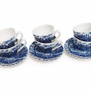 Può includere: Sei tazze e piattini bianchi con un motivo paesaggistico blu e bianco. Le tazze sono impilate e i piattini sotto. Ogni tazza ha un manico curvo.