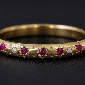 May include: A gold band ring featuring a series of flush-set round rubies and clear diamonds. Each gemstone is surrounded by a star-shaped engraving, with small circular indentations scattered across the polished gold surface of the ring.