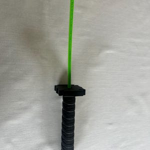 May include: A black and green measuring tool with a ridged handle and a green measuring tape extending upwards. The handle has a series of circular ridges. The measuring tape is marked with small increments.