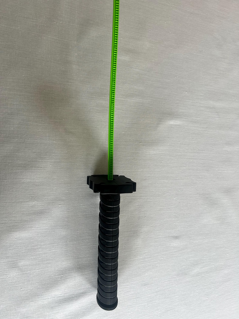 May include: A black and green measuring tool with a ridged handle and a green measuring tape extending upwards. The handle has a series of circular ridges. The measuring tape is marked with small increments.
