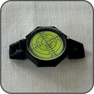 May include: A black spirit level with a circular, bubble-filled vial. The vial has a bright green background with black degree markings. The level is designed to measure angles and ensure surfaces are perfectly horizontal or vertical.