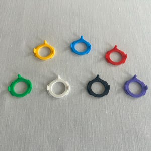 May include: Seven colorful SIM card removal tools in yellow, blue, red, green, white, black, and purple. Each tool has a circular design with a small, pointed tip.